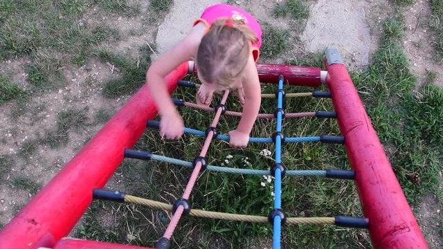 Little girl plays at playground. Small girl on climbing frame. Girl on monkey bars