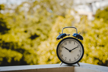 black vintage alarm clock or retro alarm clock with yellow tree leaves background