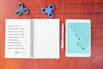 Blue graph on tablet, Pen, hand spinner, notebook on wood table background