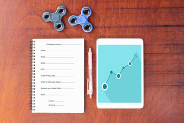 Blue graph on tablet, Pen, hand spinner, notebook on wood table background