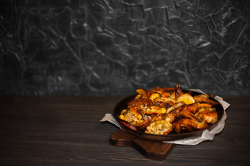 Chicken, chicken wings, fillet baked with oranges. Roast chicken and oranges on a black cast-iron frying pan on a dark background