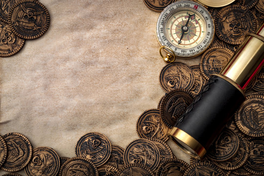 Surrender the booty and pirate raids concept with closeup on a spyglass used in the old days in navigation and exploration, compass and scattered coins on old brown paper with copy space