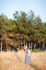 Happy senior woman in a straw hat with backpack walking through the forest. Nature outdoor activity. Healthy lifestyle concept.