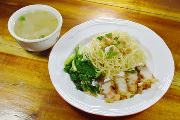 Chinese yellow noodles topping crispy pork on plate with soup