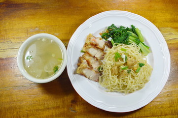 Chinese egg noodles topping crispy pork on plate with soup