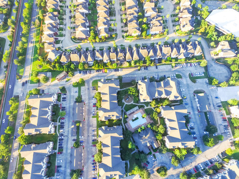 Aerial view typical multi-level apartment building next to residential houses neighborhood with swimming pool, playground, surrounded by green garden and row of cars parking lots in Houston, Texas, US