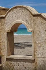 A stone arch on the walkway in Ft. Lauderdale, Florida with a view of the turquoise ocean and the beach with a shadow of a palm tree.