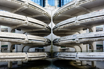 Spiral access ramps of an old decrepit concrete parking lot with a glass office building in the background.