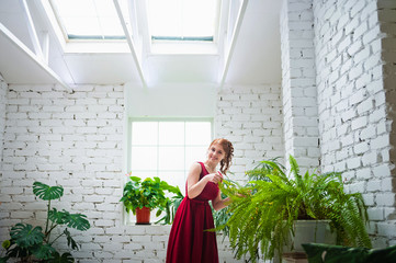 Portrait of a beautiful girl in a red dress in a loft room with plants and pallets.