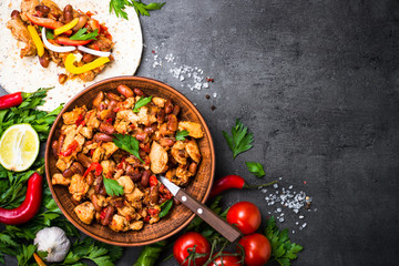 Cooking Mexican taco with meat beans and vegetables. Top view on black slate or stone background.