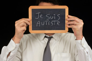 Homme cachant son visage derrière une ardoise sur laquelle est écrit je suis autiste, 