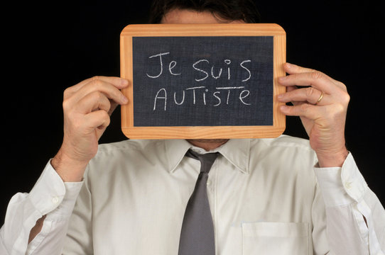 Homme cachant son visage derri&egrave;re une ardoise sur laquelle est &eacute;crit je suis autiste, 