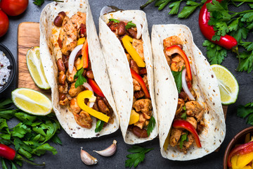 Mexican taco with meat beans and vegetables. Top view on black slate background. 