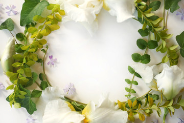 Wedding postcard. Floral frame made of Iris white flowers, buds, green ivy branches, yellow leaves and small purple flowers isolated on white. Top view. Flat lay.
