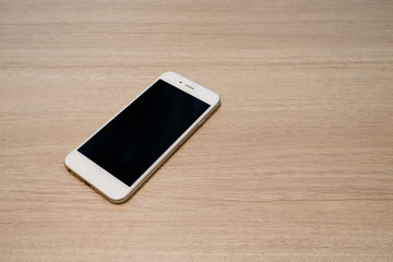 White mobile telephone lays on wooden table with copy space template backgrounds to input text