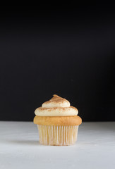 Cup cake background with single cupcake on white topped with cinnamon custard on rustic white with defocused black background - space for text