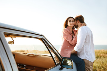Young beautiful couple embracing while leaning on a vintage car