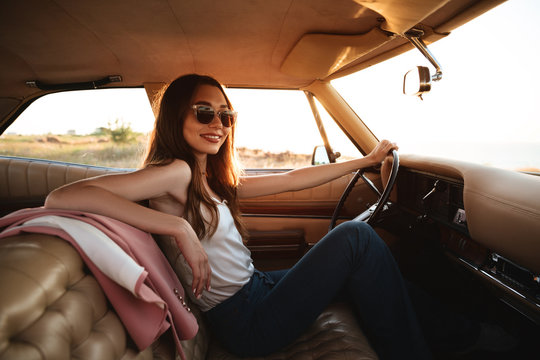 Woman in sunglasses resting while sitting inside a retro car