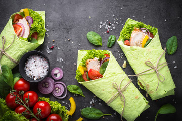 Green spinach tortilla with chicken and vegetables on black slate table. Fast food healthy snack....