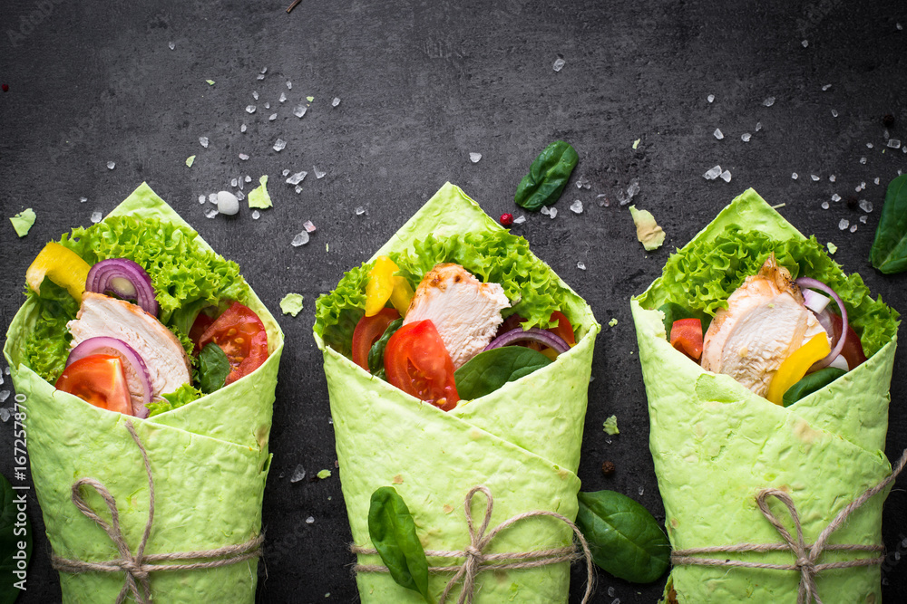 Sticker green spinach tortilla with chicken and vegetables. fast food healthy snack. top view on black slate