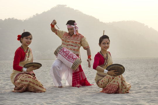 Bihu women dancing with brass plates as Bihu man plays on a dhol 