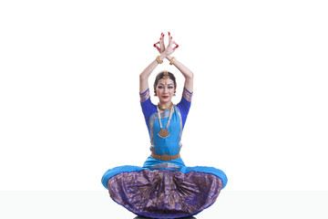 Portrait of dancer with arms raised performing Bharatanatyam against white background