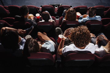 Friends sitting in cinema watch film eating popcorn