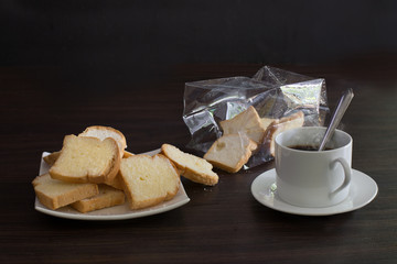 Crispy buns in white dish with hot black coffee on wooden dark background
