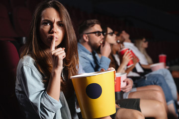 Lady sitting in cinema showing silence gesture.