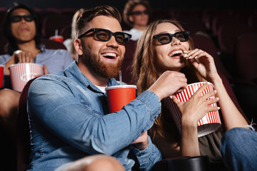 Happy friends sitting in cinema watch film eating popcorn