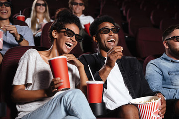 Happy friends sitting in cinema watch film eating popcorn - obrazy, fototapety, plakaty