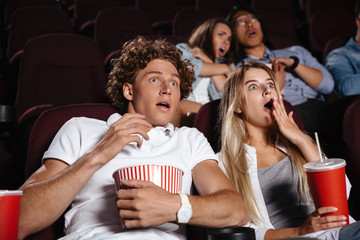 Scared young friends sitting in cinema watch film