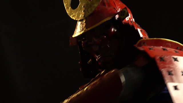 Samurai in red armor, helmet and mask waving a katana sword in front of the camera on a black background, slow motion shooting. Final attack, combo, fatality
