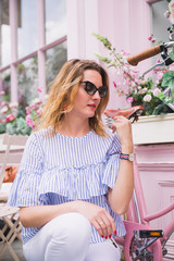 The young serious woman sits near bicycle which is interior of restaurant