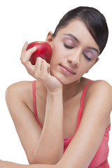 Close-up of young woman holding apple with eyes closed over white background 