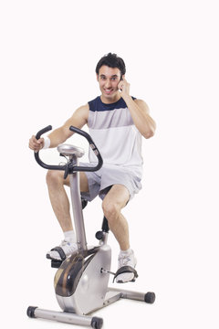 Portrait of a young man talking on mobile phone while exercising over white background 