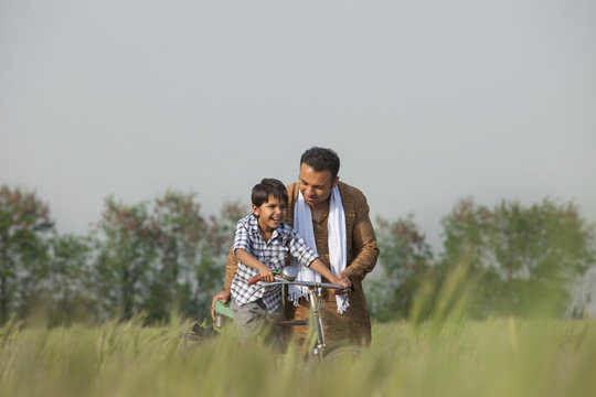 Father teaching son to ride cycle in the field 