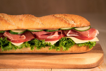 Fresh crispy sandwich with prosciutto, cheese, tomatoes, lettuce, cucumbers on a wooden background.Close Up. Healthy concept.