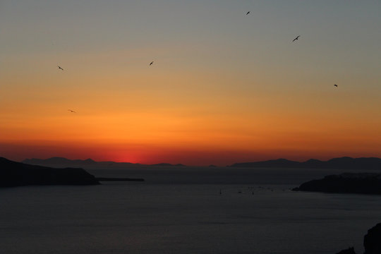 Golden Orange Sunset Views in the Greek Island of Santornini with Birds Flying in the Dark Skies