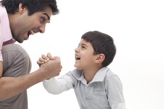 Excited father playing arm wrestle with his son over white background 