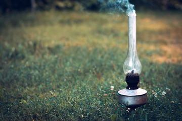 Obraz na płótnie Canvas A smoking old kerosene lamp on a green grass.