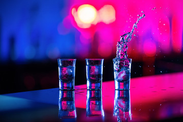  A glass of vodka with ice on the bar, on a red background © sardor_stock2