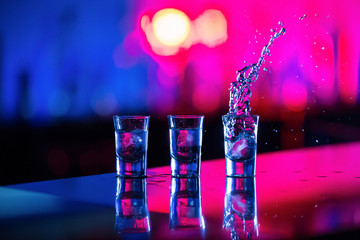  A glass of vodka with ice on the bar, on a red background