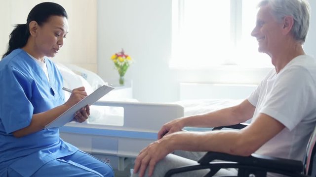 Professional nice doctor talking with a wheelchaired man