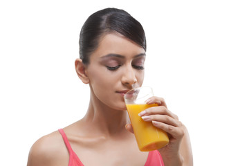 Close-up of beautiful young woman drinking orange juice over white background 