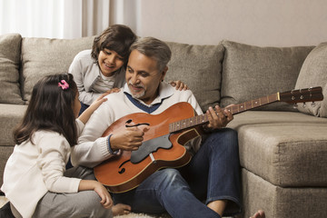 Grandfather playing guitar for grandchildren at home