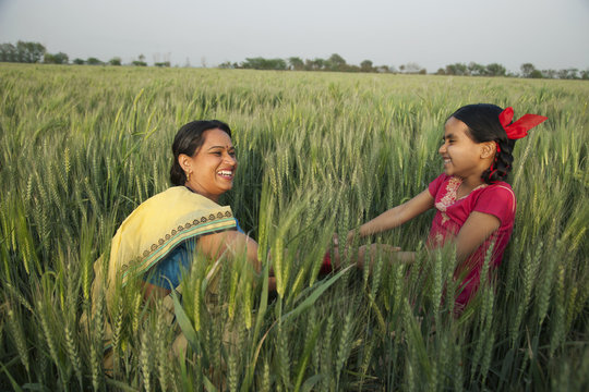 Cheerful mother and daughter playing in the wheat field 