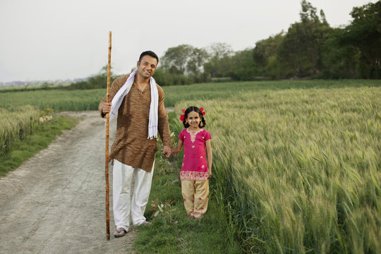 Full length portrait of father and daughter standing together in wheat field 