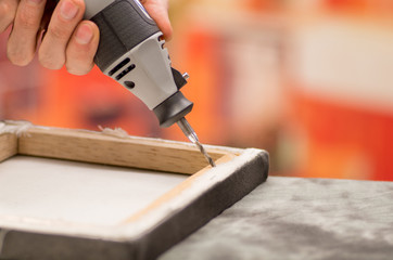 Closeup of a hardworker man drilling a wooden frame with his drill over a gray table in a blurred...