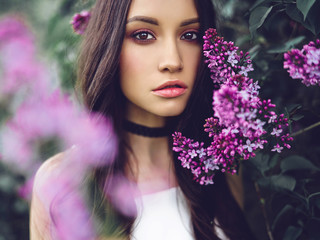 Beautiful young woman surrounded by flowers of lilac